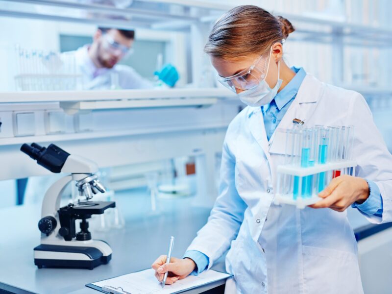 Young woman with flasks making notes in laboratory